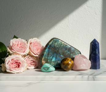 Labradorite, tiger's eye, amazonite, rose quartz and sodalite crystals on white marble with soft pink roses — crystals for reassurance seeking and self-trust by Heavenly Crystals Online.