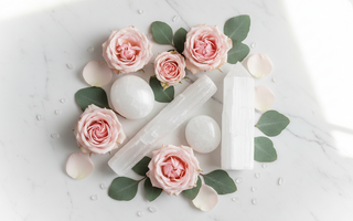Selenite wand, palm stone and tower on white marble with pink roses and eucalyptus