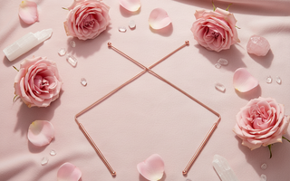 Copper dowsing rods laid on a pink surface surrounded by blush roses and rose petals, used for divination, spirit communication, and energy mapping
