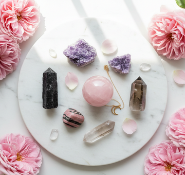 Black tourmaline, lepidolite, rose quartz, rhodonite and smoky quartz crystals on white marble with soft pink roses — healing crystals for Complex PTSD support by Heavenly Crystals Online.