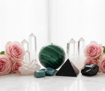 Malachite, clear quartz, shungite, amazonite and obsidian crystals on white marble with soft pink roses — healing crystals for somatic pain support by Heavenly Crystals Online