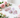 Pink and lilac Kunzite crystals in varied shapes on white marble, framed by soft pink roses.