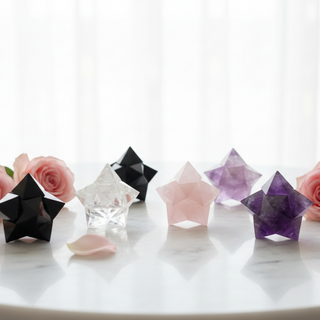 A collection of Merkabah star tetrahedron crystals in black obsidian, clear quartz, rose quartz and amethyst arranged on a white marble surface with soft pink roses