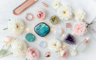 Luxury flat lay of new beginning crystals including labradorite, rainbow moonstone, chrysocolla, citrine and amethyst with blush roses and fairy lights on white marble