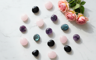 Assorted crystal palm stones and worry stones including rose quartz, amethyst, black obsidian and labradorite arranged on white marble with soft pink roses