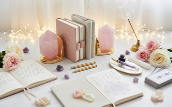 Crystal bookends, pens, journals and sacred writing tools arranged with roses and fairy lights